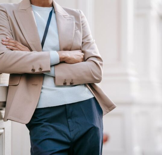 A confident woman in a classic navy blazer and tailored beige trousers walking purposefully on a city street, carrying a structured handbag, embodying easy workwear outfits for hybrid offices.