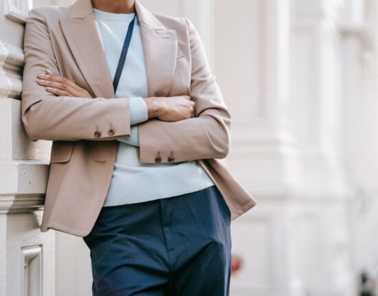A confident woman in a classic navy blazer and tailored beige trousers walking purposefully on a city street, carrying a structured handbag, embodying easy workwear outfits for hybrid offices.