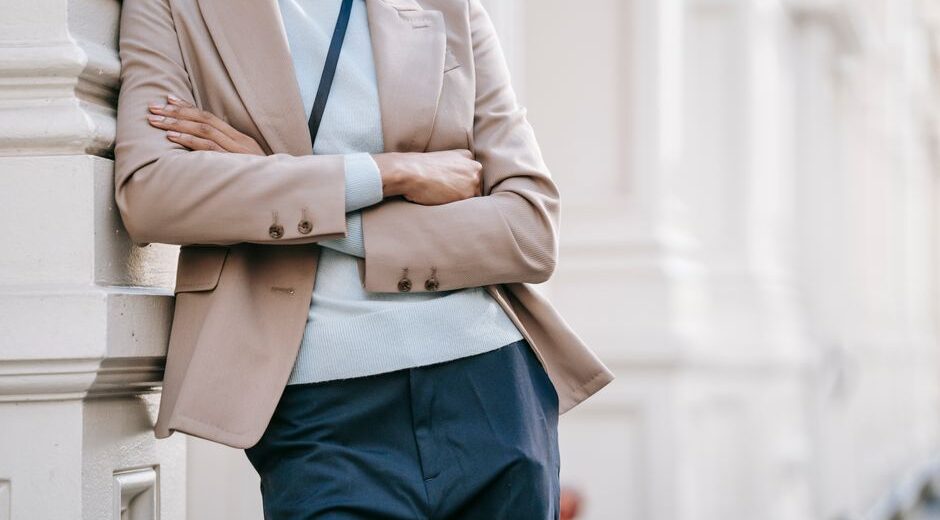 A confident woman in a classic navy blazer and tailored beige trousers walking purposefully on a city street, carrying a structured handbag, embodying easy workwear outfits for hybrid offices.