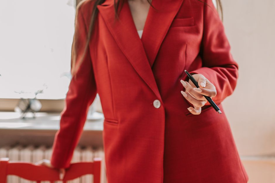 A woman in a stylish, deep green midi dress and a light grey oversized blazer stands in a minimalist office environment, showcasing a versatile and comfortable look suitable for hybrid work.