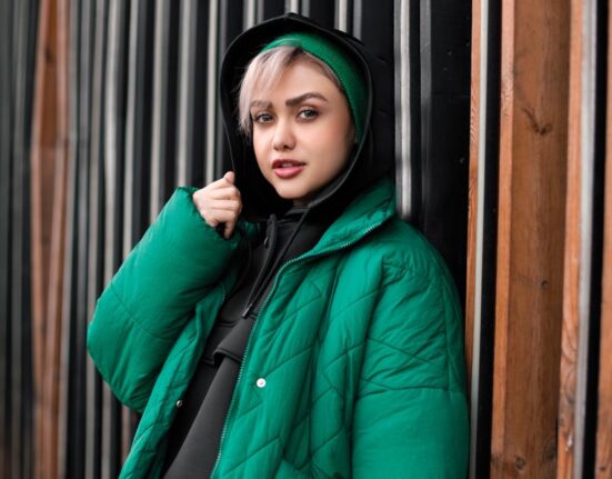 Woman wearing a chic, layered winter outfit including a tailored coat, scarf, and boots, walking confidently down a busy cold city street.