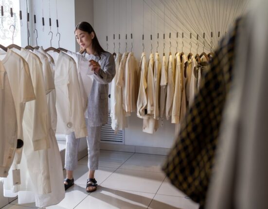 A busy woman thoughtfully considering outfit options from a neatly organized, minimalist wardrobe.