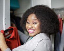 A woman looking thoughtfully at a perfectly organized, uncluttered minimalist wardrobe with neutral-colored clothes on hangers and neatly folded.