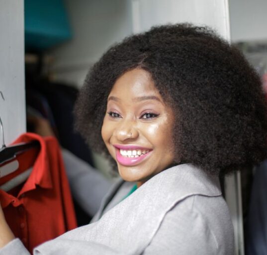 A woman looking thoughtfully at a perfectly organized, uncluttered minimalist wardrobe with neutral-colored clothes on hangers and neatly folded.