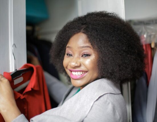 A woman looking thoughtfully at a perfectly organized, uncluttered minimalist wardrobe with neutral-colored clothes on hangers and neatly folded.