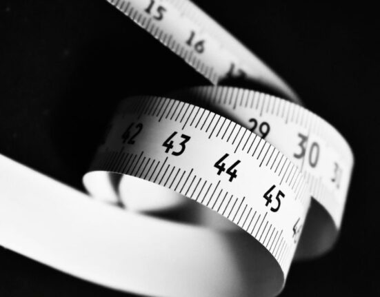 A woman carefully measuring her foot length with a ruler on a piece of paper, preparing to find her shoe size online.