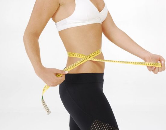 Woman using a measuring tape around her waist, in front of a laptop showing online fashion