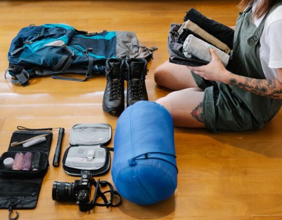 Woman thoughtfully organizing a stylish backpack with travel essentials like passport, phone, and charging cables.