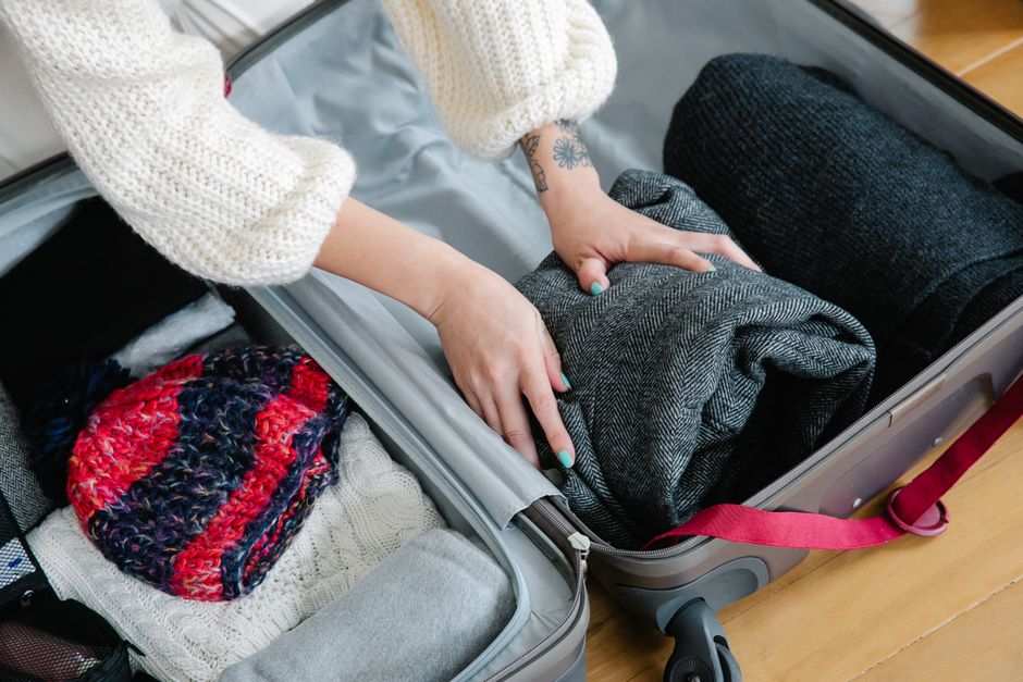 A neatly organized suitcase with a curated selection of winter clothing – a neutral coat, sweaters, thermals, and boots – showcasing a capsule wardrobe for winter travel in cold cities.