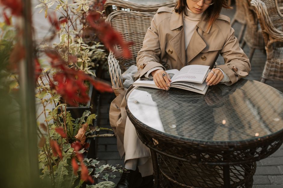 A woman sits comfortably in a cozy cafe, wearing a versatile and warm travel outfit, including a cashmere sweater and durable trousers, ideal for exploring cold cities.