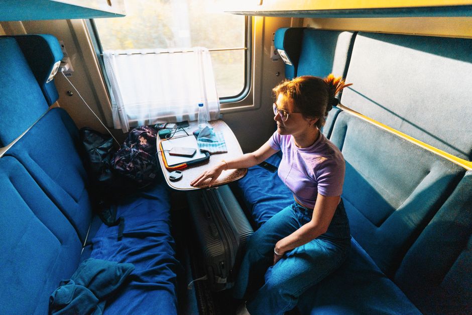 Woman sitting comfortably on a train, looking out the window, dressed in stylish yet relaxed wide-leg trousers and a soft sweater, with a book on her lap.