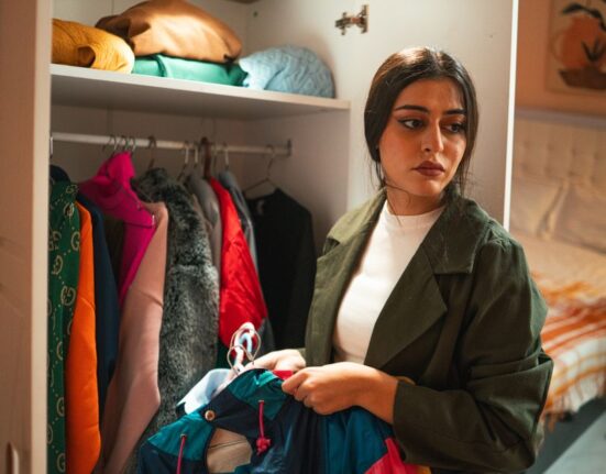 Woman thoughtfully sifting through clothing in a neatly organized, minimalist closet.