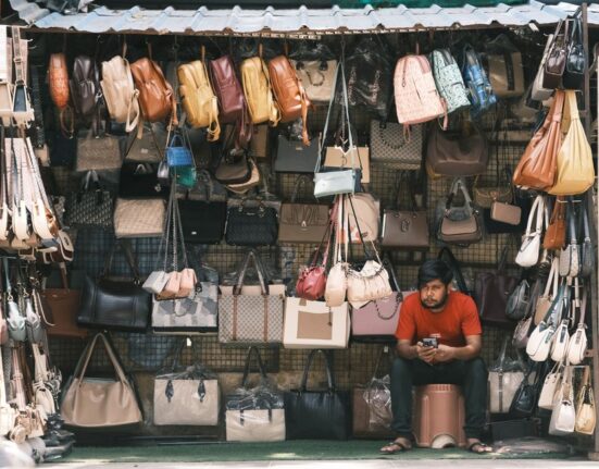 A woman comparing a sleek black vegan leather tote bag with a classic brown real leather briefcase, showcasing choices for work and travel.