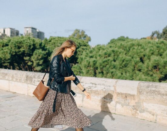 Woman wearing a black crossbody bag walking confidently through a busy European city street, hands free.