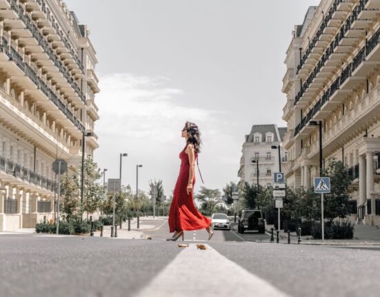 Woman in a chic, comfortable travel outfit walking along a cobblestone street in a European city, carrying a cross-body bag.