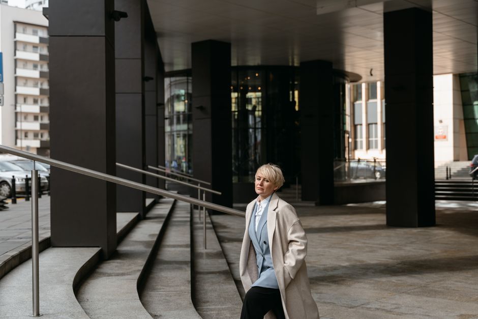 A woman in a stylish, comfortable workwear outfit (blazer, tailored trousers, smart shoes) walking confidently on a city street.