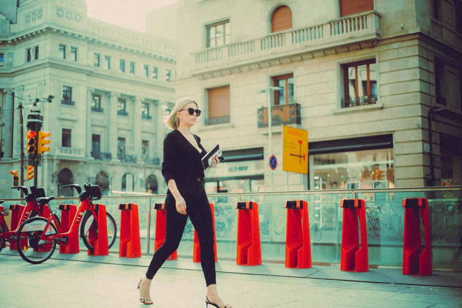 A woman confidently walking down a bustling European city street, dressed in a smart casual outfit that balances comfort and style, suitable for travel or an evening out.