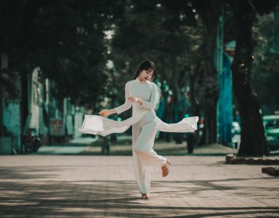 A woman confidently walks down a sunny, humid city street, dressed in a breezy white linen midi dress and comfortable sandals, demonstrating stylish women's summer outfits for humid weather.