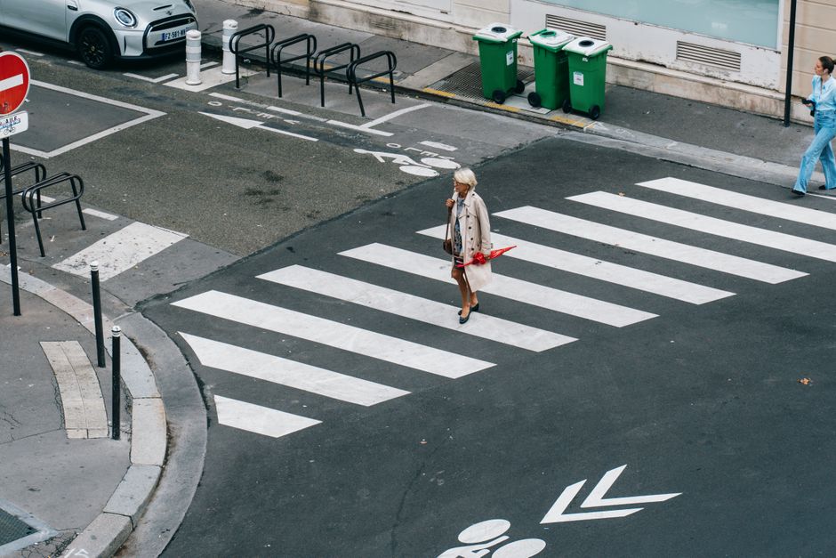 Stylish woman in a beige trench coat, jeans, and comfortable shoes walking past a Parisian cafe.