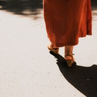 A woman in comfortable walking sandals strolling down a sunlit historic European street, highlighting freedom from foot pain.