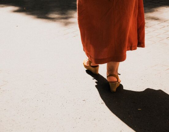 A woman in comfortable walking sandals strolling down a sunlit historic European street, highlighting freedom from foot pain.