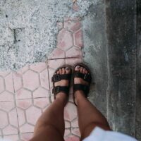 A woman wearing stylish yet supportive walking sandals strolling comfortably on an old cobblestone street, highlighting the importance of proper footwear for European travel.