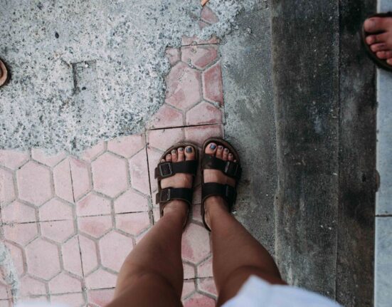 A woman wearing stylish yet supportive walking sandals strolling comfortably on an old cobblestone street, highlighting the importance of proper footwear for European travel.
