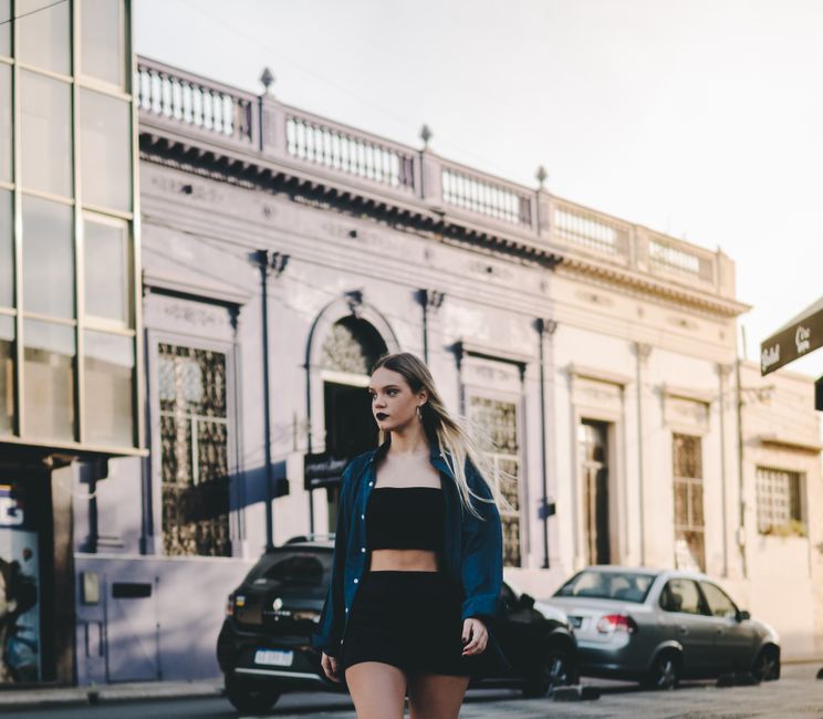 A woman confidently walking through a European city street, wearing a stylish yet comfortable travel outfit with a light jacket and comfortable shoes.