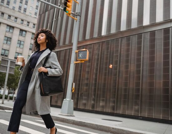Woman with a stylish vegan leather crossbody bag walking through a vibrant European city street.