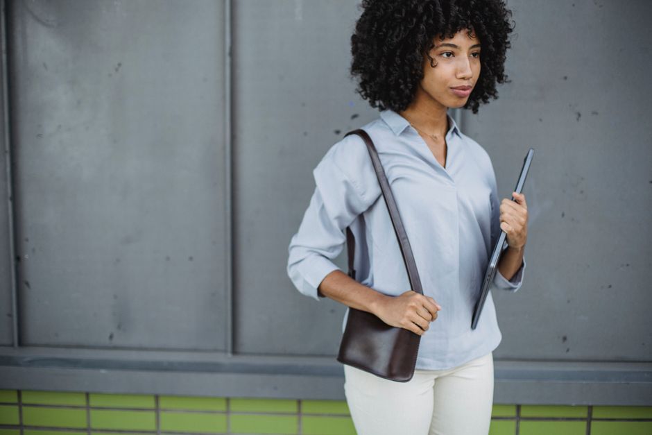 Professional woman walking through a European city street, carrying a laptop tote bag and a crossbody bag, looking comfortable and secure.