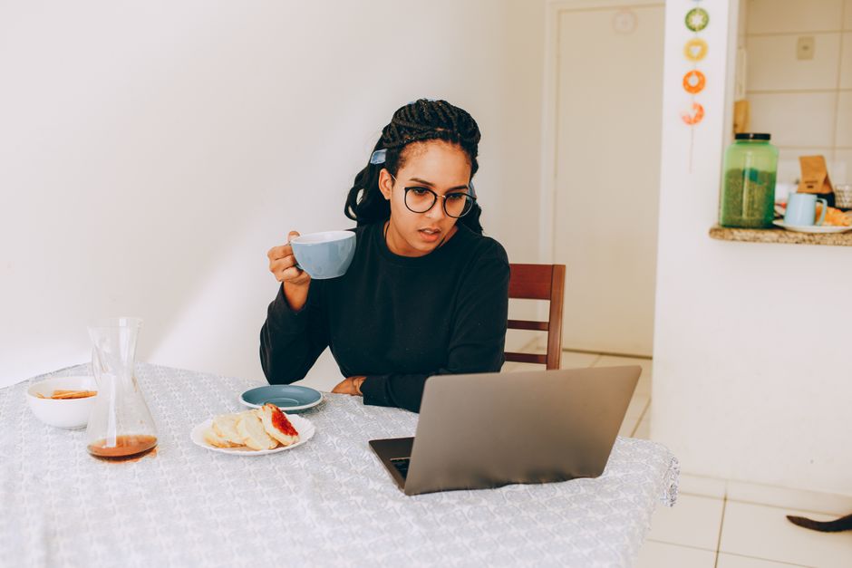 A woman smiling while working comfortably at her home desk, dressed in a soft, elegant knit top, illustrating the comfort aspect of hybrid workwear.